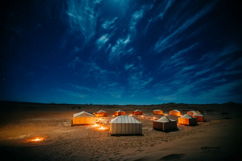 Campo tendato illuminato nel deserto sotto il cielo notturno